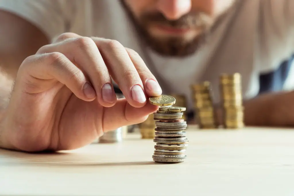 Man counting coins and placing a coin on top of a pile of pound coins