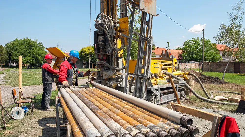 Drilling geothermal well for a residential geothermal heat pump. Workers on Drilling Rig. A worker prepares to join two pieces of drill pipe on a drilling rig.